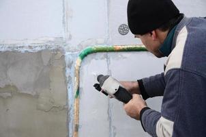 un ouvrier âgé perce un trou dans un mur en polystyrène pour l'installation ultérieure d'une cheville de renfort en plastique. créer des trous dans le mur avec une perceuse. réchauffement de la façade du bâtiment photo