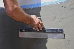 mains d'un vieux travailleur manuel avec des outils de plâtrage de mur rénovant la maison. plâtrier rénovant les murs extérieurs et les coins avec spatule et plâtre. isolation des murs. travaux de finition du bâtiment photo