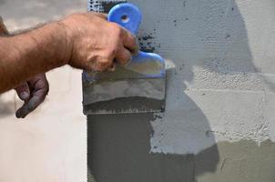 mains d'un vieux travailleur manuel avec des outils de plâtrage de mur rénovant la maison. plâtrier rénovant les murs extérieurs et les coins avec spatule et plâtre. isolation des murs. travaux de finition du bâtiment photo