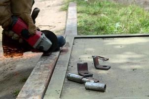 meulage de roue électrique sur structure en acier à l'extérieur. ancien travailleur manuel dans des gants de protection coupant une porte en métal avec une meuleuse photo