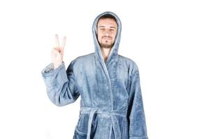 portrait d'un jeune homme barbu caucasien en peignoir bleu montre un geste de victoire ou de paix isolé sur fond blanc photo