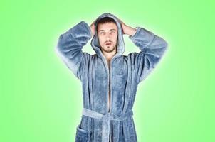 portrait d'un jeune homme barbu caucasien en peignoir bleu montre une émotion de visage confus isolée sur fond vert photo