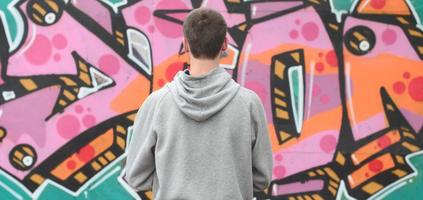 un jeune graffeur dans un sweat à capuche gris regarde le mur avec photo