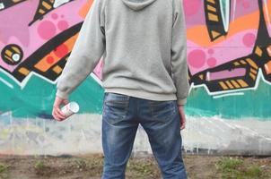 un jeune graffeur dans un sweat à capuche gris regarde le mur avec photo