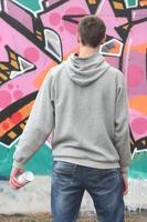 un jeune graffeur dans un sweat à capuche gris regarde le mur avec photo