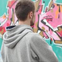 un jeune graffeur dans un sweat à capuche gris regarde le mur avec photo