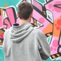 un jeune graffeur dans un sweat à capuche gris regarde le mur avec photo