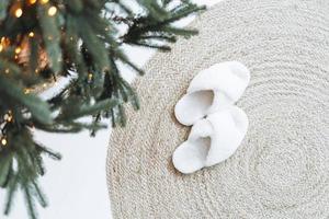 chaussons moelleux confortables sur un tapis naturel près de l'arbre de noël photo