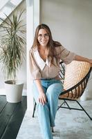 portrait d'une jeune femme souriante aux cheveux longs assise sur une chaise dans un bureau moderne photo