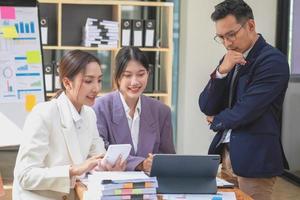 L'équipe commerciale asiatique se compose de personnel de marketing. le comptable et le responsable financier s'entraident pour analyser les bénéfices de l'entreprise à l'aide de tablettes. calculatrices, ordinateurs portables, papier millimétré et stylos d'entreprise. photo