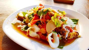 salade épicée thaïlandaise en gros plan mélangée à du calmar frais, de la saucisse thaïlandaise, de la coquille, des crevettes, des tranches de tomate, de la carotte, de l'oignon, du piment, de l'ail, du bok choy et de l'eau citronnée. célèbre cuisine asiatique pour l'alimentation et la santé.