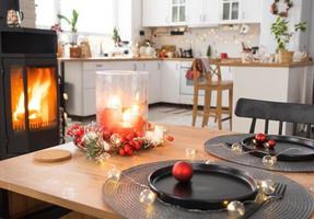 l'intérieur festif de la maison est décoré pour noël et le nouvel an dans un style loft avec poêle noir, cheminée, arbre de noël. chambre studio chaleureuse avec table dressée, feu de bois, cosy et chauffage d'accueil photo