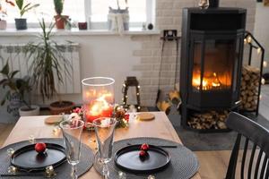 l'intérieur festif de la maison est décoré pour noël et le nouvel an dans un style loft avec poêle noir, cheminée, arbre de noël. chambre studio chaleureuse avec table dressée, feu de bois, cosy et chauffage d'accueil photo