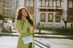 jeune femme utilisant un smartphone dans la rue et tenant un café à emporter photo