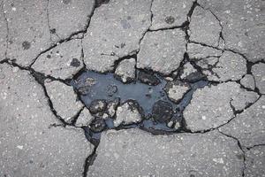 grandes fissures sur la route goudronnée remplie d'eau, dommages à la surface de la route au printemps photo