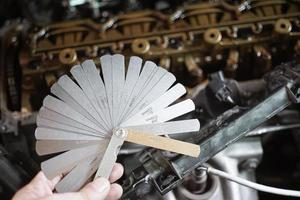 mécanicien automobile à l'aide d'une jauge d'épaisseur régler la soupape de la voiture. mesure du jeu des soupapes avec jeu de jauges d'épaisseur de poussoir photo