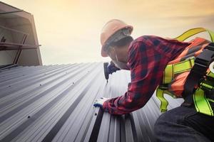 couvreur en uniforme de protection et gants, outils de toiture, installation de nouveaux toits en construction, perceuse électrique utilisée sur les nouveaux toits avec tôle. photo