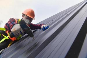 gros plan perceuse couvreur en uniforme de protection et gants, outils de toiture, installation de nouveaux toits en construction, perceuse électrique utilisée sur les nouveaux toits avec tôle. photo