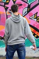 un jeune graffeur dans un sweat à capuche gris regarde le mur avec photo