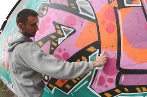 un jeune homme dans un sweat à capuche gris peint des graffitis en rose et vert c photo