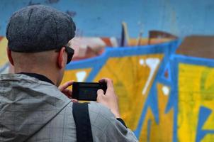 un jeune graffeur photographie son image terminée sur le mur. le gars utilise la technologie moderne pour capturer un dessin de graffiti abstrait coloré. se concentrer sur l'appareil photo