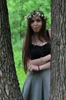 portrait d'une jeune fille émotive avec une couronne de fleurs sur la tête et des ornements brillants sur le front. jolie brune posant dans une belle forêt en plein essor pendant la journée par beau temps photo