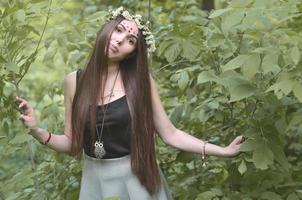 une photo de forêt d'une belle jeune brune d'apparence européenne aux yeux marron foncé et aux grandes lèvres. sur la tête de la jeune fille porte une couronne de fleurs, sur son front des décorations brillantes