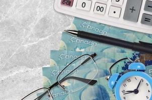 Billets de 5 dollars canadiens et calculatrice avec lunettes et stylo. prêt commercial ou concept de saison de paiement des impôts. le temps de payer les impôts photo
