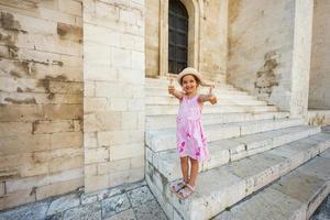 happy baby girl tourist show thumbs up against basilique saint nicolas à bari, pouilles, italie du sud. photo