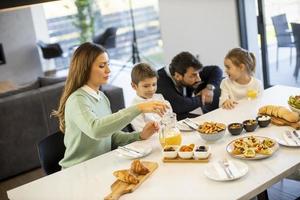 jeune famille heureuse parlant tout en prenant son petit déjeuner à table à manger photo