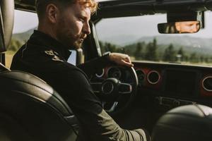 jeune homme aux cheveux roux conduisant un véhicule tout terrain lors d'un roadtrip dans la nature photo