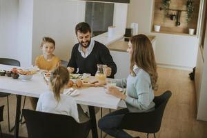 jeune famille heureuse parlant tout en prenant son petit déjeuner à table à manger photo