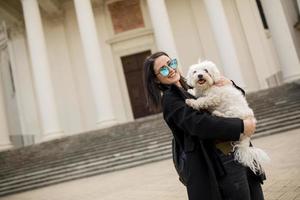 belle jeune femme heureuse avec un mignon petit chien chiot s'amuser dans la rue photo