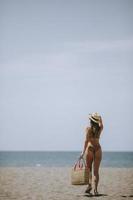 jeune femme en bikini avec sac de paille sur la plage au jour d'été photo