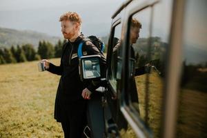 jeune homme se détendre et boire du café par le capot du véhicule tout-terrain à la campagne photo