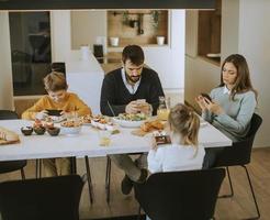 famille utilisant des téléphones portables tout en prenant son petit déjeuner à la table à manger de l'appartement photo