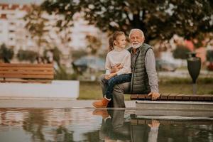grand-père passe du temps avec sa petite-fille au bord d'une petite piscine d'eau dans le parc le jour de l'automne photo