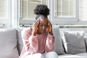 jeune femme noire déprimée assise sur un canapé bouleversée ayant des problèmes de relations personnelles, une fille afro-américaine du millénaire stressée touche la tête se sent désespérée en deuil ou en deuil de la perte photo