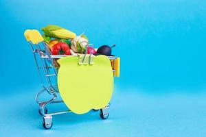 panier en métal avec fruits et légumes sur fond bleu. caddie miniature jouet photo