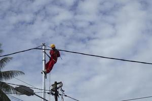 Gorontalo-Indonésie, décembre 2022 - des techniciens connectent des câbles aux poteaux électriques. Employé suspendu par ceinture sur poteau électrique pour la pose de câbles basse tension photo