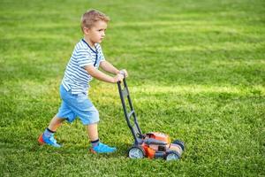 Heureux garçon de 3 ans s'amusant à tondre la pelouse photo