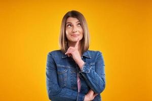 gros plan d'une femme en veste en jean pensant et pointant sur fond jaune photo