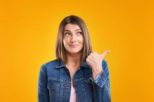 gros plan d'une femme en veste en jean pensant et pointant sur fond jaune photo