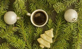 café de noël. une tasse de café, deux boules d'argent de noël et un jouet de sapin doré sur fond de sapin, vue de dessus. photo