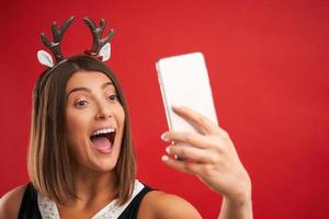 femme heureuse adulte dans l'ambiance de Noël prenant selfie sur fond rouge photo