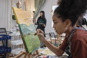 une fille afro-américaine se concentre sur la peinture acrylique sur toile avec un groupe d'étudiants en classe d'art, l'apprentissage créatif avec des talents et des compétences dans l'enseignement en studio à l'école primaire. photo