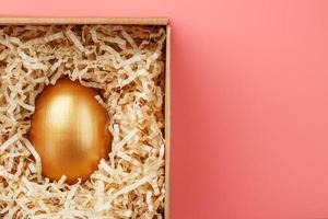 oeuf d'or dans une boîte sur fond rose. le concept d'exclusivité, meilleur choix, prix, surprise spéciale, cadeau coûteux. photo