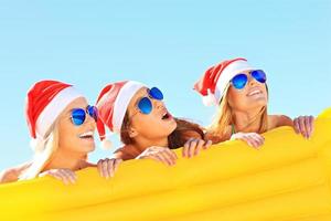 groupe de filles en chapeaux de père noël s'amusant sur la plage photo