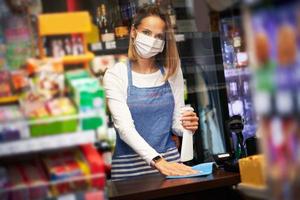 vendeuse désinfectant les surfaces d'une épicerie photo