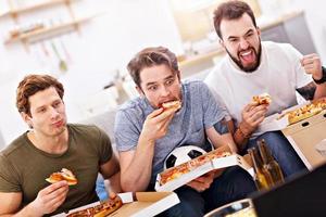 heureux amis masculins mangeant de la pizza et regardant la télévision photo